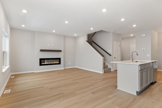 kitchen featuring light wood-style flooring, recessed lighting, gray cabinets, a sink, and a glass covered fireplace