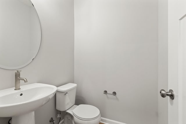 half bathroom featuring toilet, baseboards, and a sink