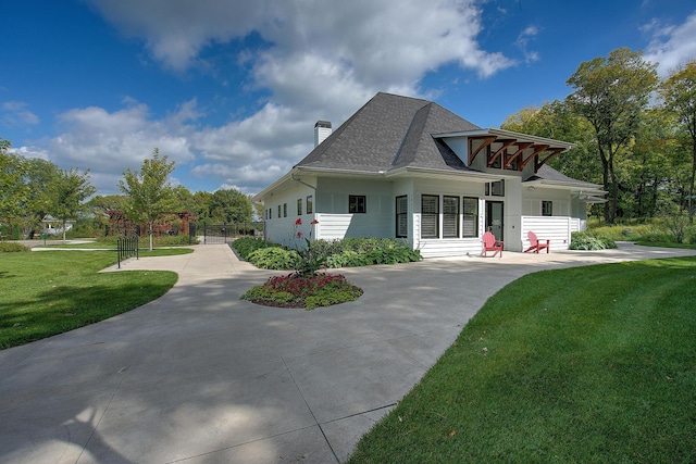 back of house with a lawn, roof with shingles, concrete driveway, and a chimney