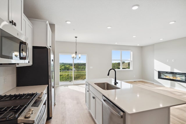 kitchen featuring a sink, stainless steel appliances, light wood-style floors, a glass covered fireplace, and tasteful backsplash