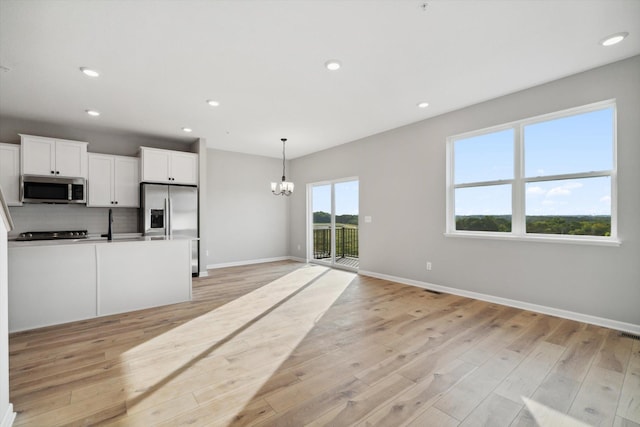 kitchen with a notable chandelier, decorative backsplash, stainless steel appliances, and light wood-type flooring