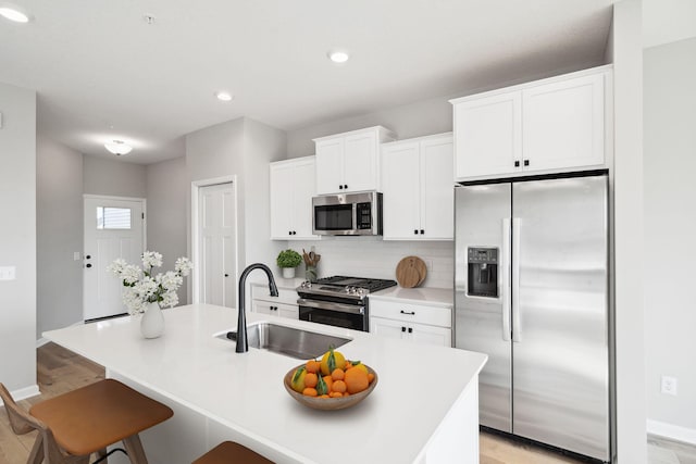 kitchen with a center island with sink, a sink, appliances with stainless steel finishes, white cabinetry, and tasteful backsplash