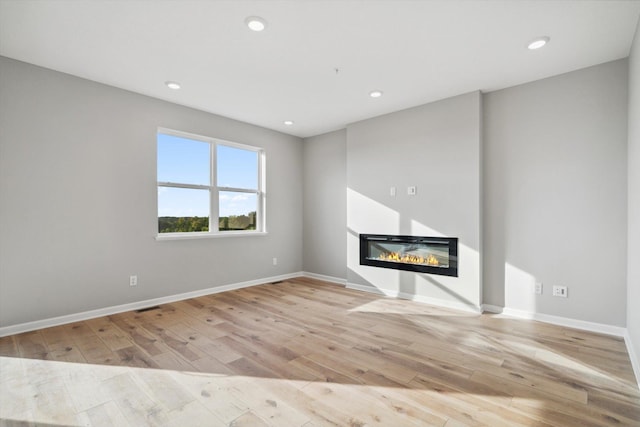 unfurnished living room with a glass covered fireplace, baseboards, wood finished floors, and recessed lighting