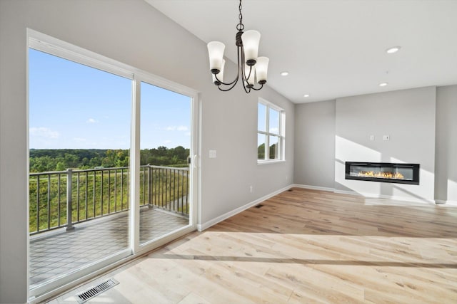 unfurnished living room with wood finished floors, baseboards, recessed lighting, a glass covered fireplace, and a notable chandelier