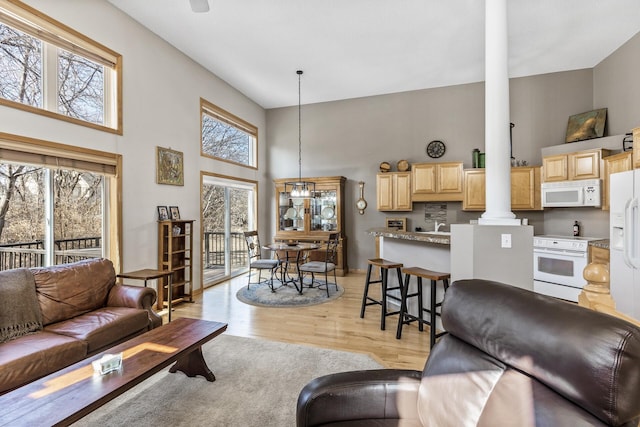 living room featuring a high ceiling, light wood finished floors, and ornate columns