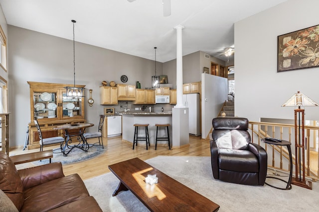 living area featuring stairs, light wood-style floors, a towering ceiling, and a ceiling fan