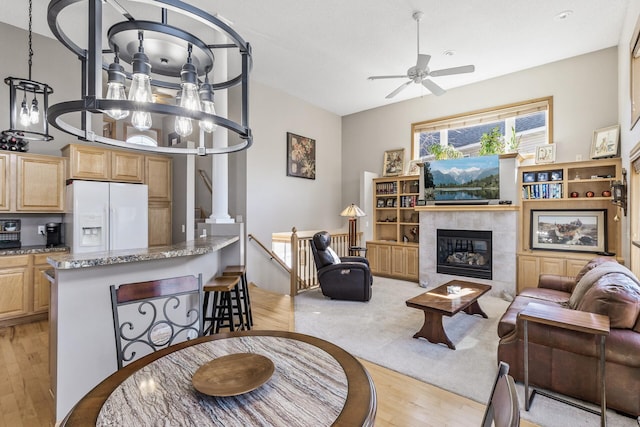 living area featuring a tiled fireplace, light wood-style flooring, and ceiling fan with notable chandelier