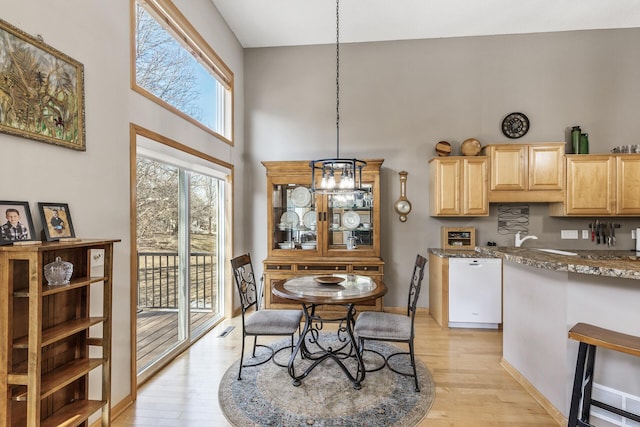 dining room featuring baseboards, light wood-type flooring, a towering ceiling, and a chandelier