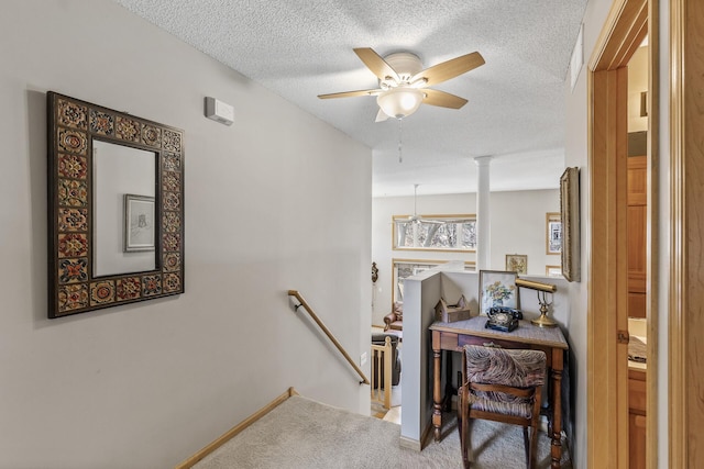 interior space featuring an upstairs landing, a textured ceiling, carpet flooring, decorative columns, and baseboards