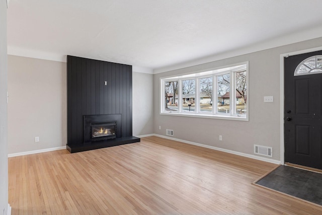 entryway with light wood finished floors, visible vents, a large fireplace, and baseboards