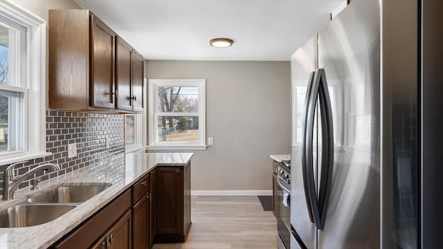 kitchen featuring a sink, backsplash, appliances with stainless steel finishes, light wood finished floors, and baseboards