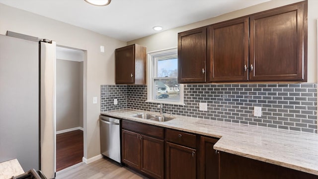 kitchen featuring light stone countertops, dark brown cabinetry, decorative backsplash, stainless steel appliances, and a sink