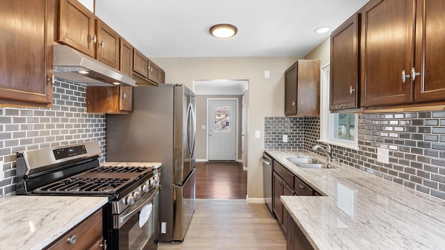 kitchen featuring under cabinet range hood, light stone counters, appliances with stainless steel finishes, and a sink