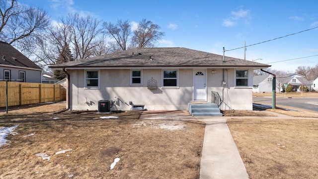 view of front of property with central air condition unit, a shingled roof, stucco siding, and fence