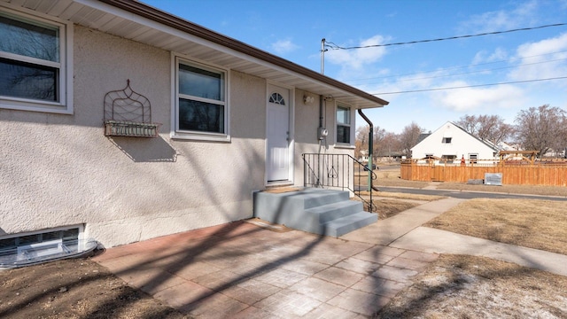 doorway to property featuring stucco siding and fence