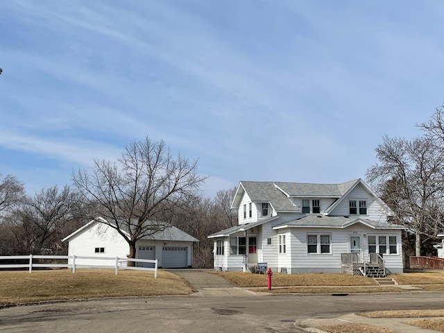 view of front of house featuring a garage, an outbuilding, roof with shingles, and fence