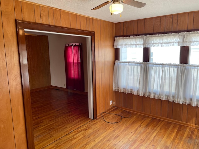 empty room featuring wooden walls, a textured ceiling, ceiling fan, and hardwood / wood-style floors