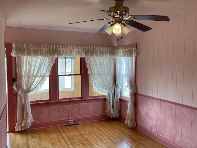 spare room with a ceiling fan, a healthy amount of sunlight, baseboards, and wood-type flooring