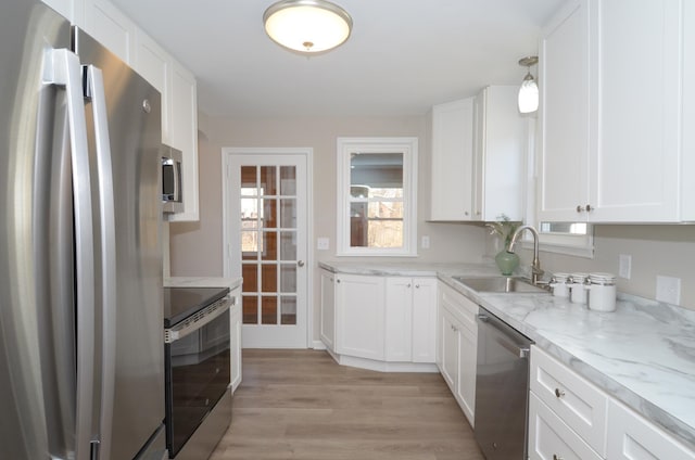 kitchen with light wood-type flooring, light stone counters, white cabinets, stainless steel appliances, and a sink