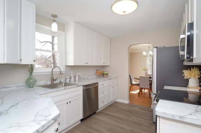 kitchen with a sink, arched walkways, appliances with stainless steel finishes, white cabinets, and light wood finished floors