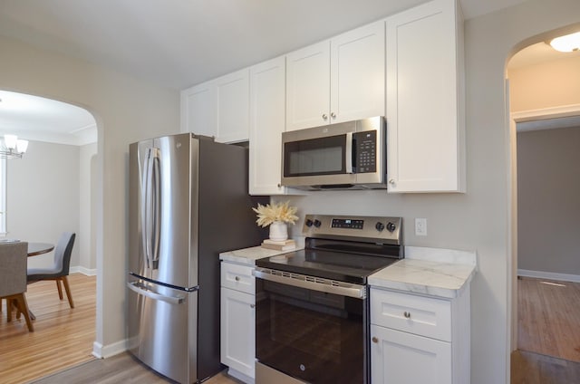 kitchen featuring light wood finished floors, baseboards, appliances with stainless steel finishes, an inviting chandelier, and white cabinetry