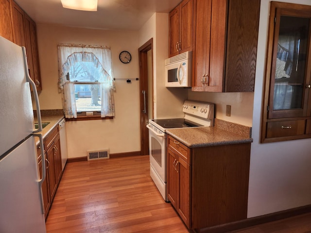 kitchen featuring visible vents, baseboards, brown cabinets, light wood-style floors, and white appliances