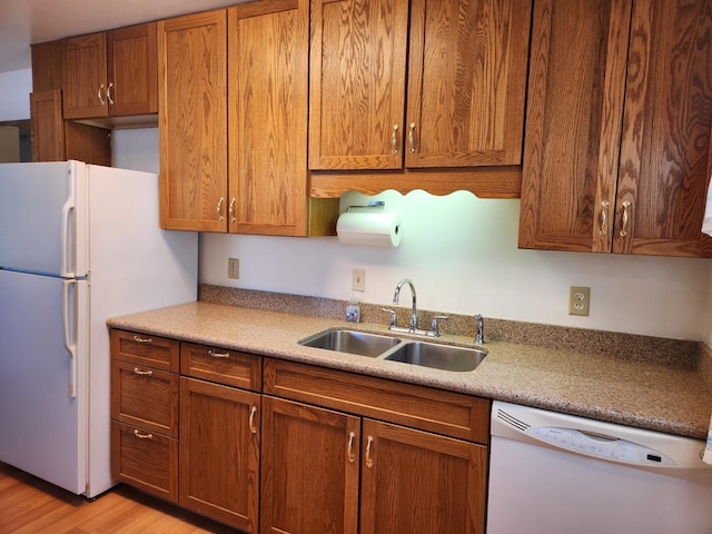 kitchen with light wood finished floors, light countertops, brown cabinets, white appliances, and a sink