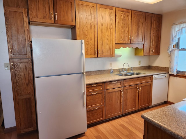 kitchen with white appliances, brown cabinetry, light wood-style flooring, a sink, and light countertops