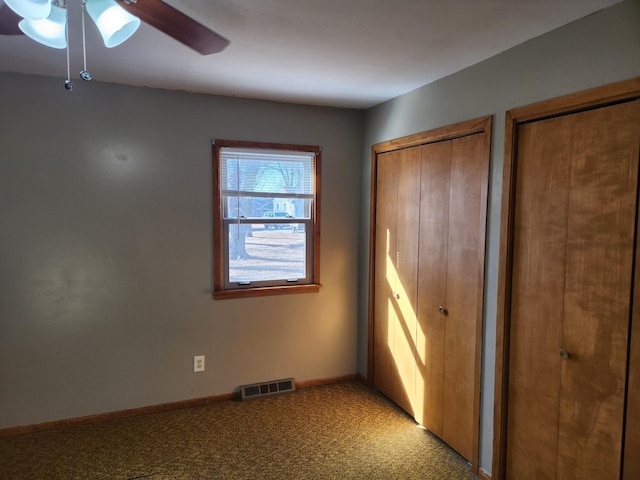 unfurnished bedroom featuring visible vents, baseboards, multiple closets, light colored carpet, and a ceiling fan