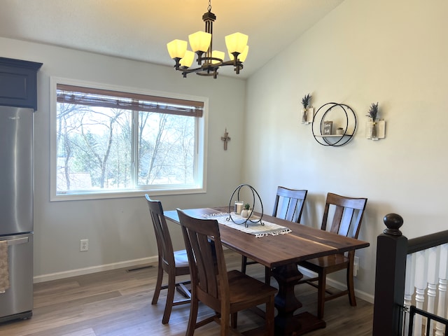 dining area featuring vaulted ceiling, a notable chandelier, wood finished floors, and baseboards