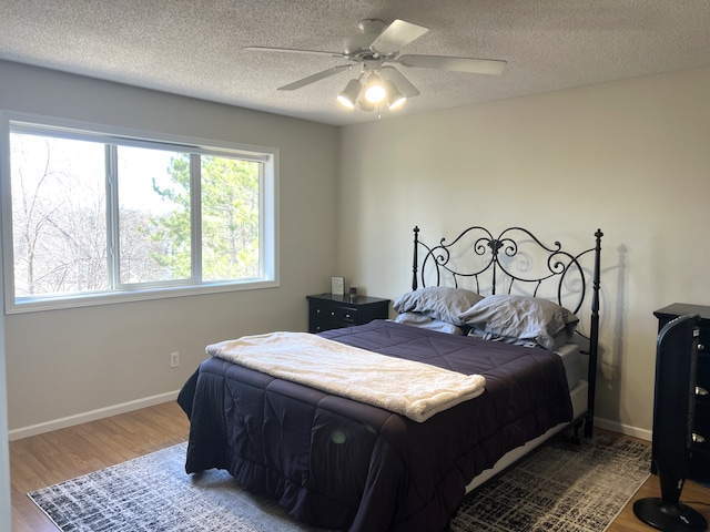 bedroom featuring ceiling fan, a textured ceiling, baseboards, and wood finished floors