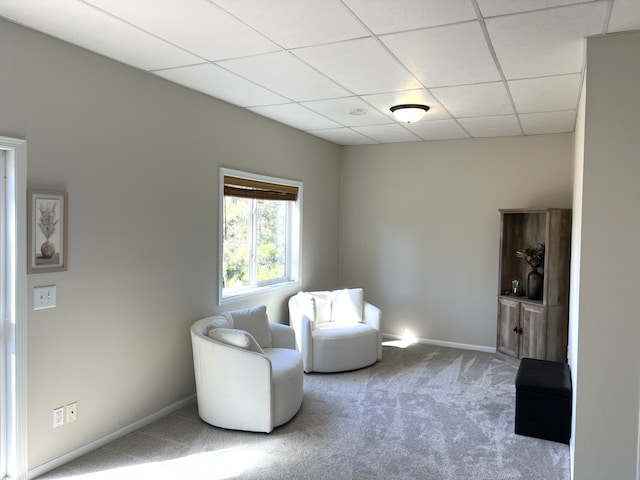 living area featuring carpet, baseboards, and a drop ceiling