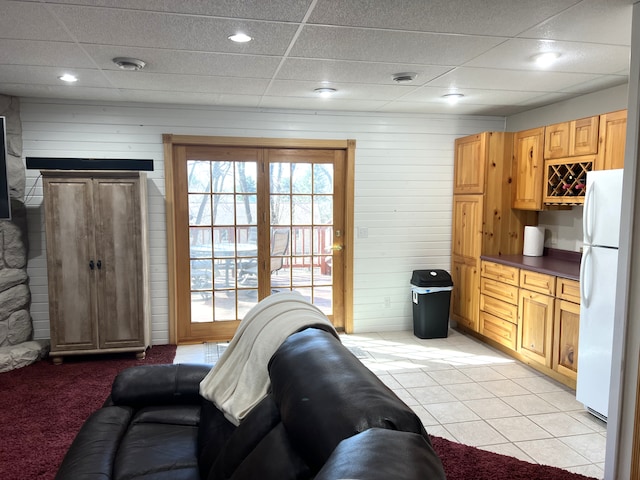 living area with a drop ceiling, light tile patterned flooring, and wood walls