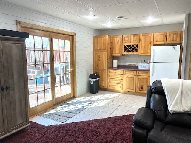 kitchen featuring wooden walls, light tile patterned flooring, a drop ceiling, freestanding refrigerator, and dark countertops