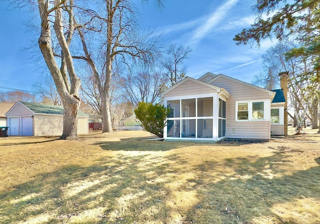 back of house featuring a yard, an outbuilding, a chimney, and a sunroom