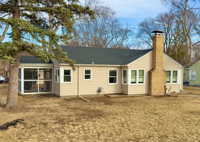 rear view of house with a shingled roof, a sunroom, and a chimney