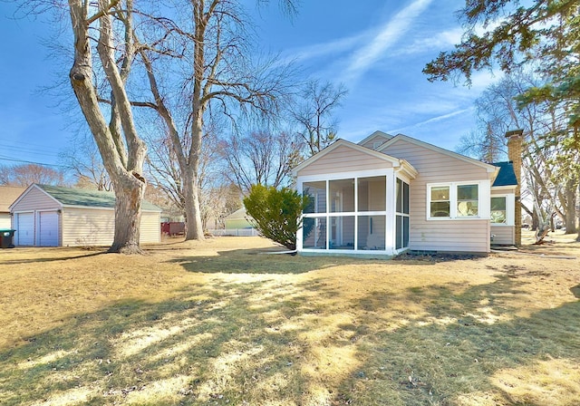 rear view of house featuring a lawn, a chimney, an outdoor structure, and a sunroom