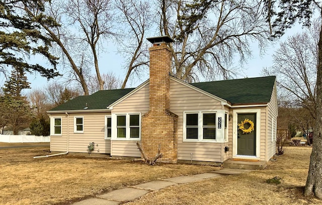 view of front of house featuring entry steps, a chimney, a front lawn, and a shingled roof