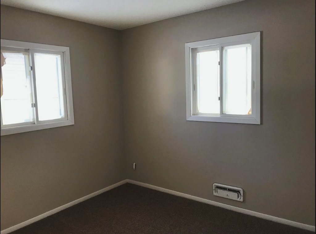 empty room with plenty of natural light, dark carpet, and baseboards