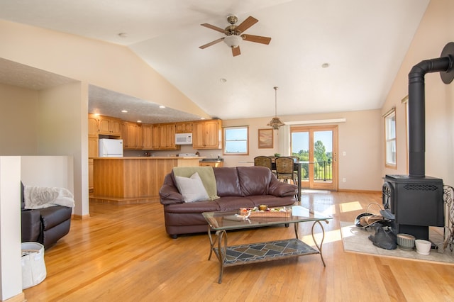 living room with a ceiling fan, baseboards, high vaulted ceiling, a wood stove, and light wood-type flooring