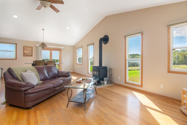 living room featuring light wood finished floors, a wood stove, baseboards, and vaulted ceiling