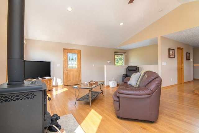 living area featuring vaulted ceiling, recessed lighting, light wood-style flooring, a wood stove, and a ceiling fan