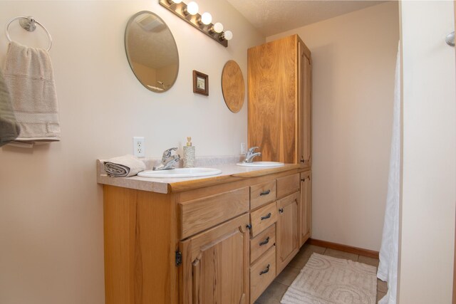 bathroom featuring tile patterned flooring, double vanity, baseboards, and a sink