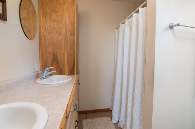 bathroom featuring tile patterned flooring, double vanity, baseboards, and a sink