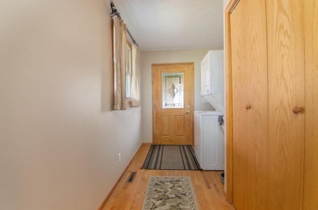 doorway to outside featuring visible vents, light wood-style flooring, stacked washer and clothes dryer, and baseboards