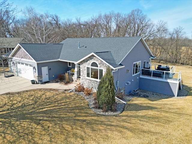 exterior space with driveway, roof with shingles, an attached garage, a yard, and stone siding