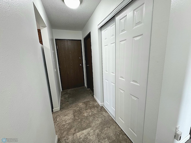 hallway with stone finish floor, baseboards, and a textured ceiling