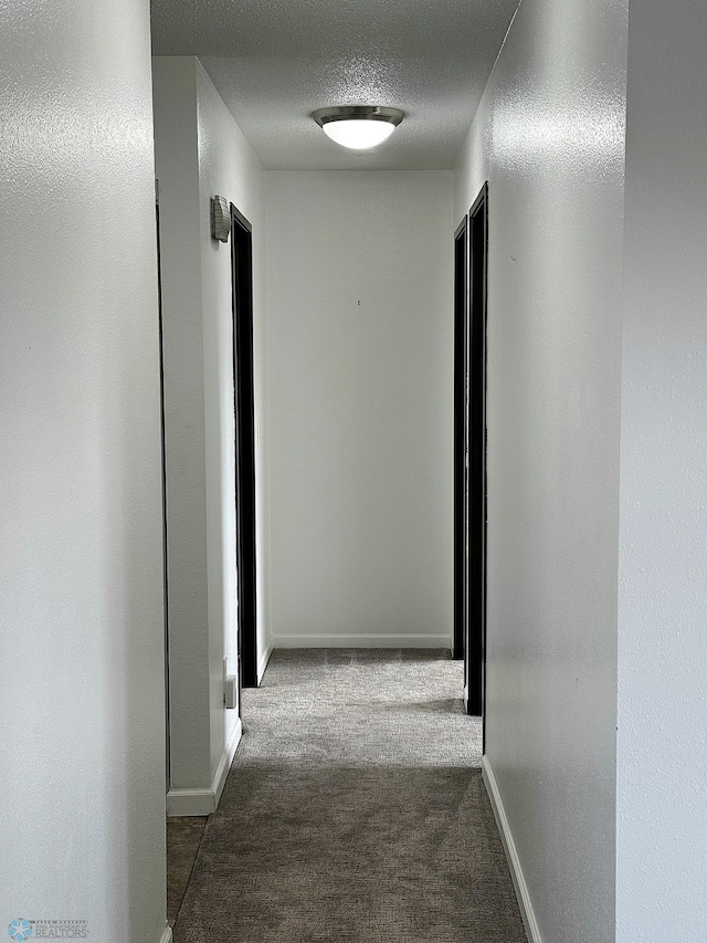 hallway featuring dark colored carpet, baseboards, and a textured ceiling