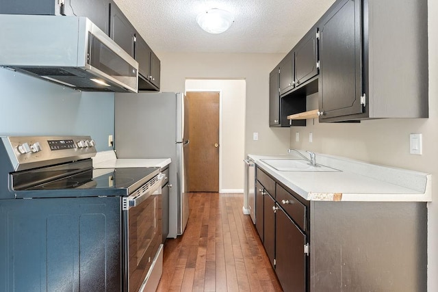 kitchen featuring hardwood / wood-style floors, a sink, stainless steel appliances, light countertops, and a textured ceiling