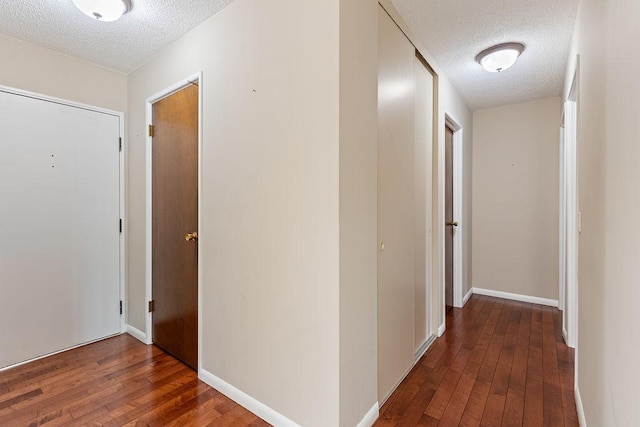 hall with baseboards, a textured ceiling, and hardwood / wood-style flooring